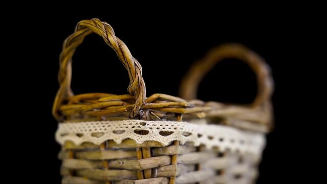 Stylish vintage wicker basket with small handles decorated with white lace strip turns on black background extreme closeup