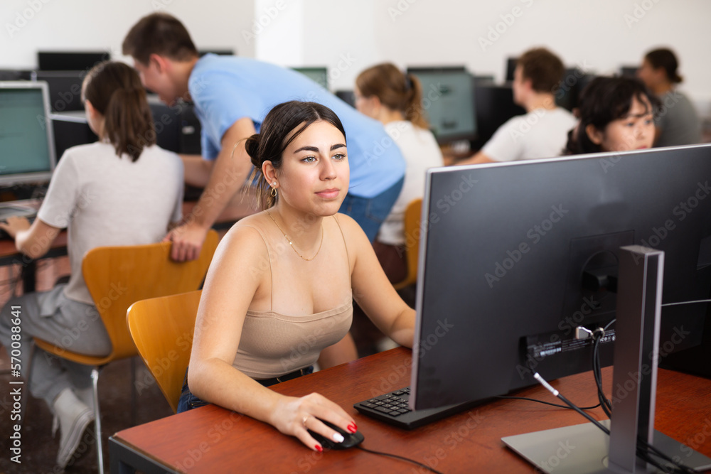 Poster smart latin female teenager learning computer science while she is using a pc in the computer classr