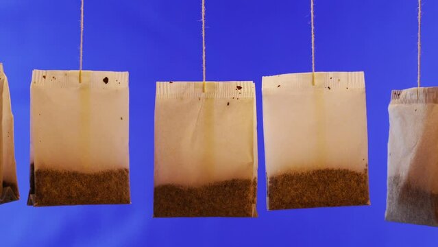 Collection of used paper tea bags with herbal brew hang waving on thin threads against deep blue wall extreme close view
