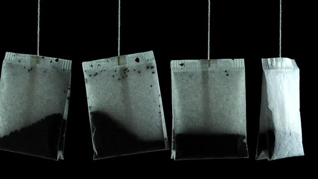Group of new white dry paper tea bags with tasty natural brew hang on thin threads on black background extreme close view
