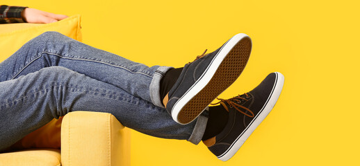 Stylish man in shoes and jeans pants sitting in armchair on yellow background