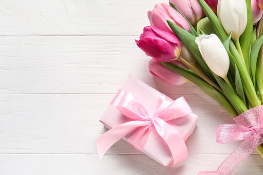 Bouquet of beautiful tulip flowers and gift box on light wooden background