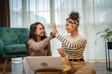 Two friends or sisters or girlfriends are using laptop to do shopping online in their apartment
