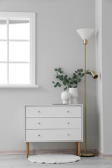 White chest of drawers with vases and lamp near light wall