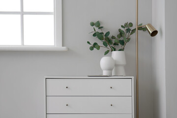 White chest of drawers with vases and lamp near light wall