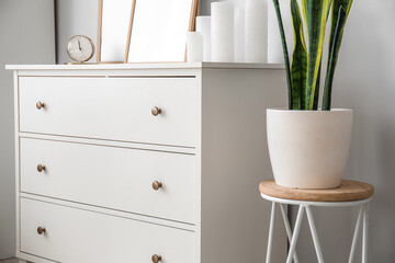 Chest of drawers with blank frames, alarm clock and candles in light living room