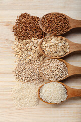 Spoons with different cereals on wooden background, closeup