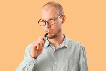 Young man in eyeglasses smoking disposable electronic cigarette on beige background
