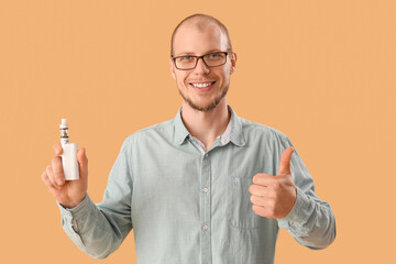 Young man in eyeglasses with disposable electronic cigarette showing thumb-up on beige background