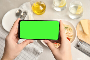 Chroma key compositing. Woman holding smartphone with green screen at table indoors, closeup....