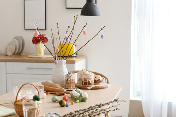 Vase with tree branches, Easter cakes and eggs on dining table in kitchen