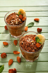Glasses of delicious chocolate pudding with almond, banana and mint on green wooden table
