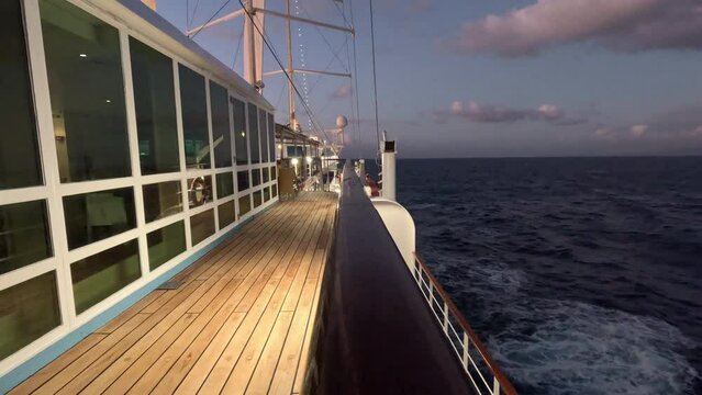 Lighted amber teakwood Cruise ship deck looking aft at passing sea in early dusk as the sea grows dark - Empty, vacant deck