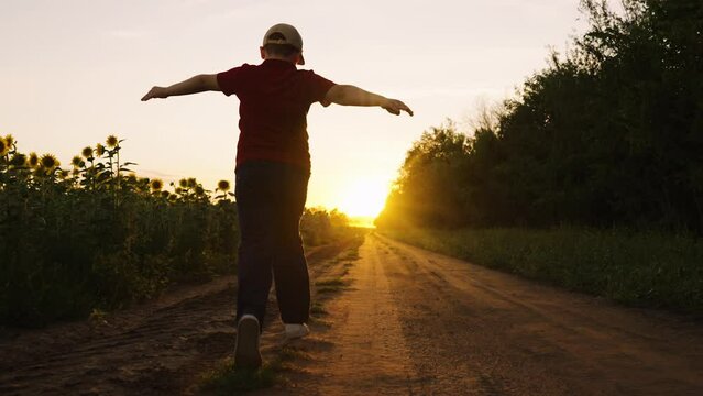 Child pilot runs through field of sunflowers, kid dreams, airplane pilot. Child runs with his arms raised like wings of an airplane, childhood dream travel, nature. Silhouette of boy running at sunset