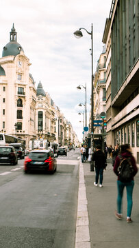 Vertical photo os a parisian street with cars being driven by the road and a walkway crowded of people walking to work at first hour in the morning  