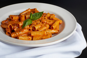 Classic Penne all Vodka. Italian ziti pasta covered in sauce garnished with a sprig of basil. White plate and napkin. 