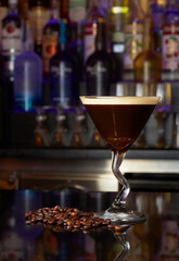Espresso Martini Coffee-flavored cocktail in a zig-zag martini glass with coffee beans.Bar and bottles in the background. White light on background.