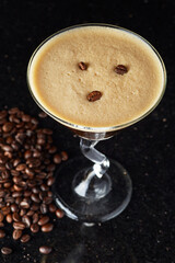 Espresso Martini Coffee-flavored cocktail in a zig-zag martini glass. Black background with coffee beans.