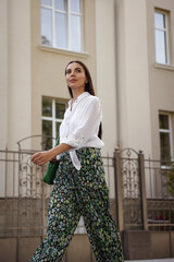 Beautiful young woman in stylish outfit walking on city street