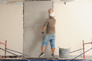 Worker installing tile on wall indoors, back view