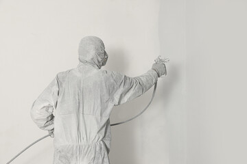 Decorator in uniform painting wall with sprayer indoors, back view