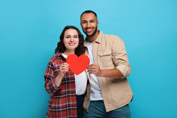 Lovely couple with red paper heart on light blue background. Valentine's day celebration