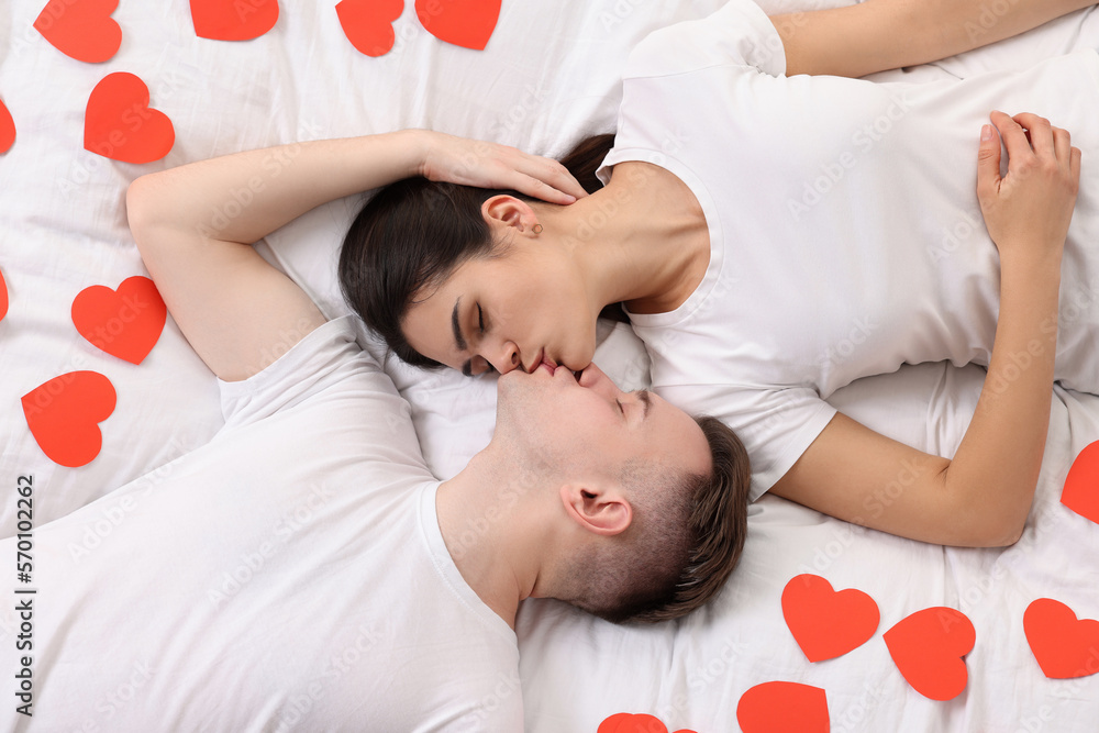 Poster Lovely couple kissing on bed with many decorative hearts, top view. Valentine's day celebration