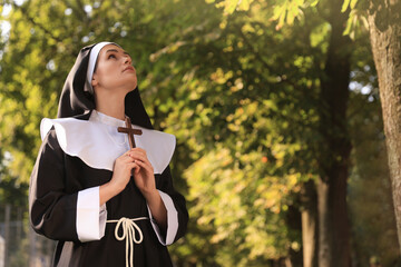 Young nun with Christian cross in park on sunny day, space for text