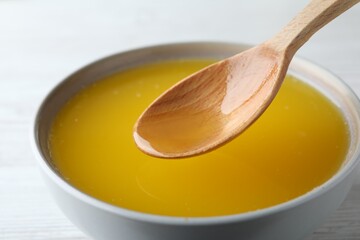 Spoon of clarified butter over bowl on white table, closeup