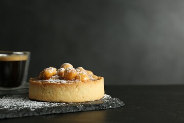 Delicious tart with hazelnuts, sweet caramel and powdered sugar on black table. Space for text