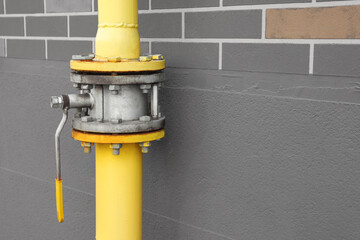 Yellow gas pipe with valve near brown wall outdoors, space for text