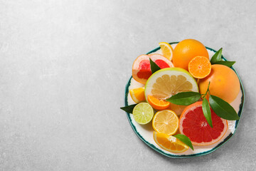 Plate with different citrus fruits and fresh leaves on light grey table, top view. Space for text