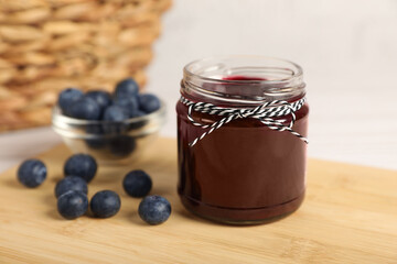 Jar with tasty blueberry jam and berries on wooden table. Space for text
