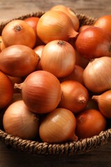 Wicker basket with many ripe onions on table, closeup