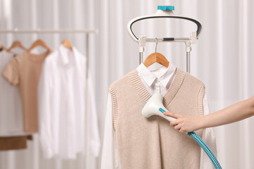 Woman steaming clothes on hanger at home, closeup. Space for text - obrazy, fototapety, plakaty