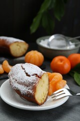 Piece of delicious homemade yogurt cake with powdered sugar and tangerines on gray table