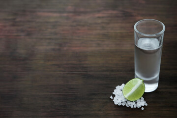 Mexican tequila shot with lime slice and salt on wooden table, space for text. Drink made from agave