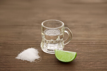 Mexican tequila shot with lime slice and salt on wooden table, closeup. Drink made from agave