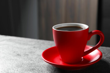 Red cup with aromatic coffee on grey textured table indoors, closeup. Space for text
