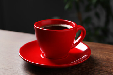 Red cup with aromatic coffee on wooden table indoors, closeup