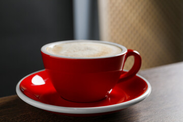 Red cup with aromatic cappuccino on wooden table indoors, closeup