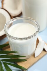 Obraz na płótnie Canvas Glass of delicious vegan milk, coconuts and leaf on light blue background, closeup