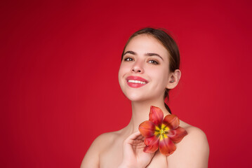 Obraz na płótnie Canvas Beauty girl with tulip near naked shoulder. Beautiful sensual woman hold tulips, studio portrait on red background.