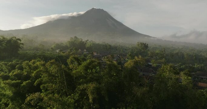Aerial Shot Of Active Volcano Mountain By Residential Hill, Drone Flying Forward Over Green Trees During Sunset - Java, Indonesia