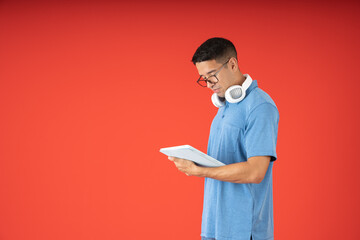 Young man wearing glasses, reading on a digital tablet and wearing headphones on his neck
