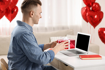 Valentine's day celebration in long distance relationship. Man holding gift box while having video...