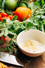 Chopped garlic in a white bowl, vegetables in the background