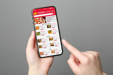 Food delivery service. Woman choosing dish from menu on site using smartphone on grey background,...