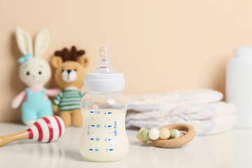 Feeding bottle with milk and other baby accessories on white table near beige wall. Space for text