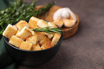 Delicious crispy croutons in bowl and rosemary on dark table, closeup. Space for text